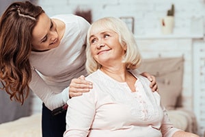 Caregiver with hands on shoulders of seated elderly woman